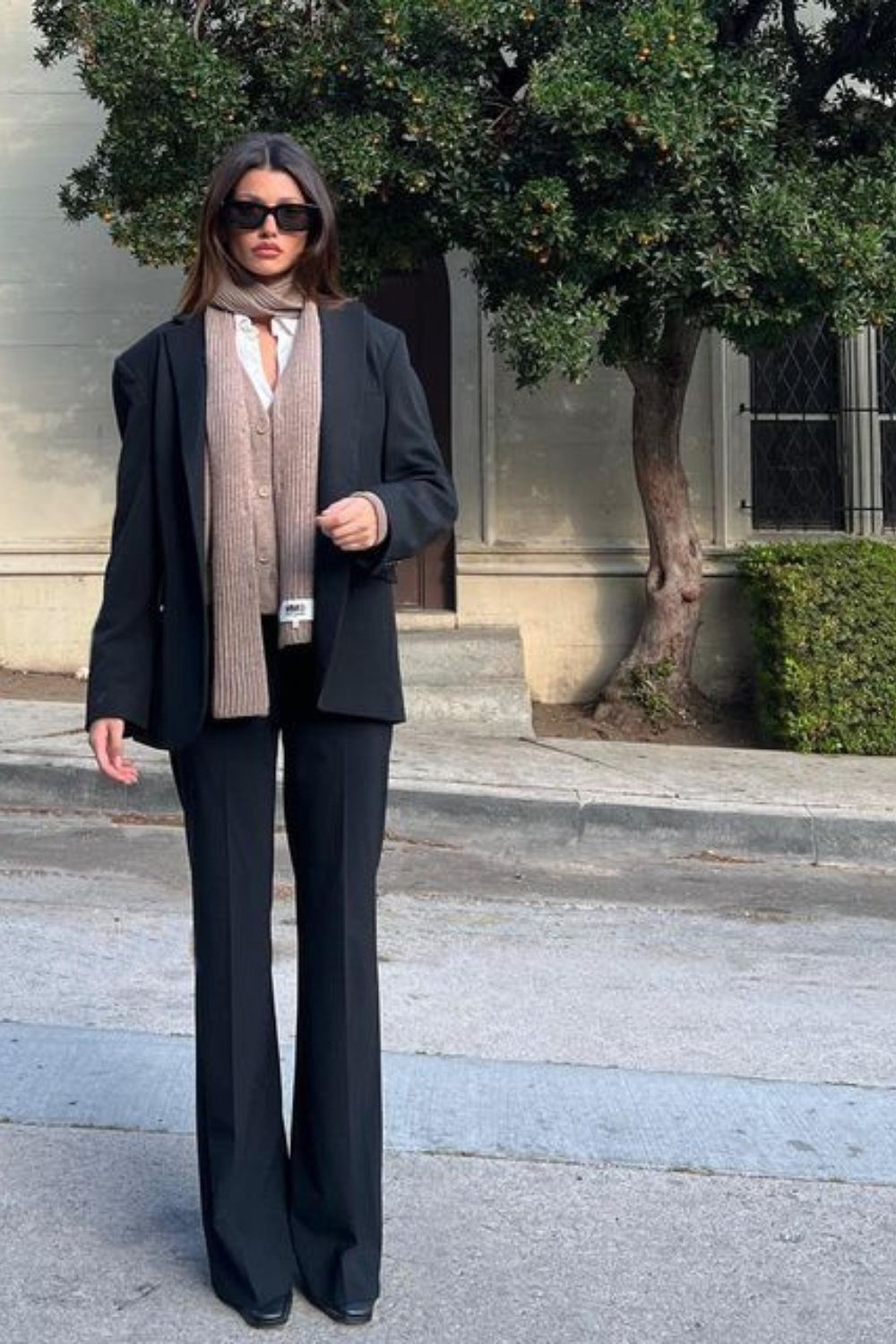 Woman wearing a black blazer and flared trousers with a tan scarf.