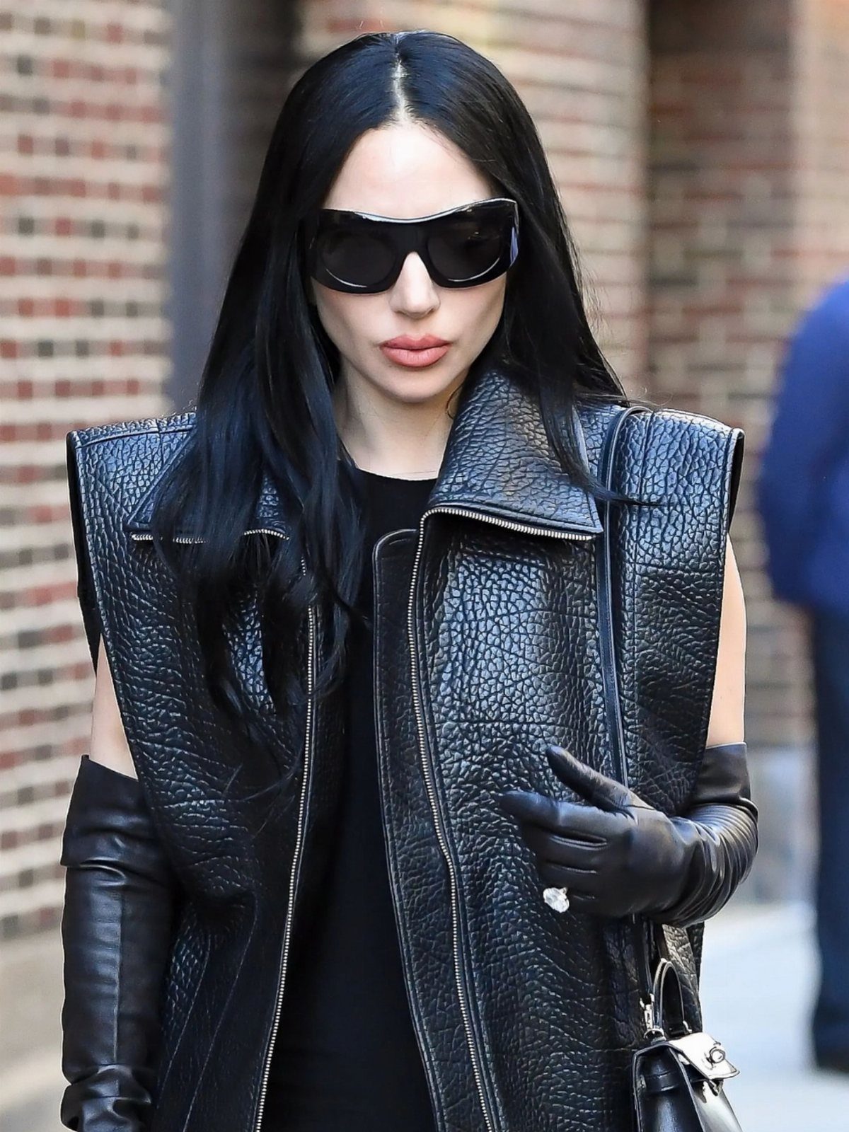 11 Lady Gaga Outfits That Defined Her Style Evolution 10 Lady Gaga wearing a black leather vest, long gloves, and oversized black sunglasses.