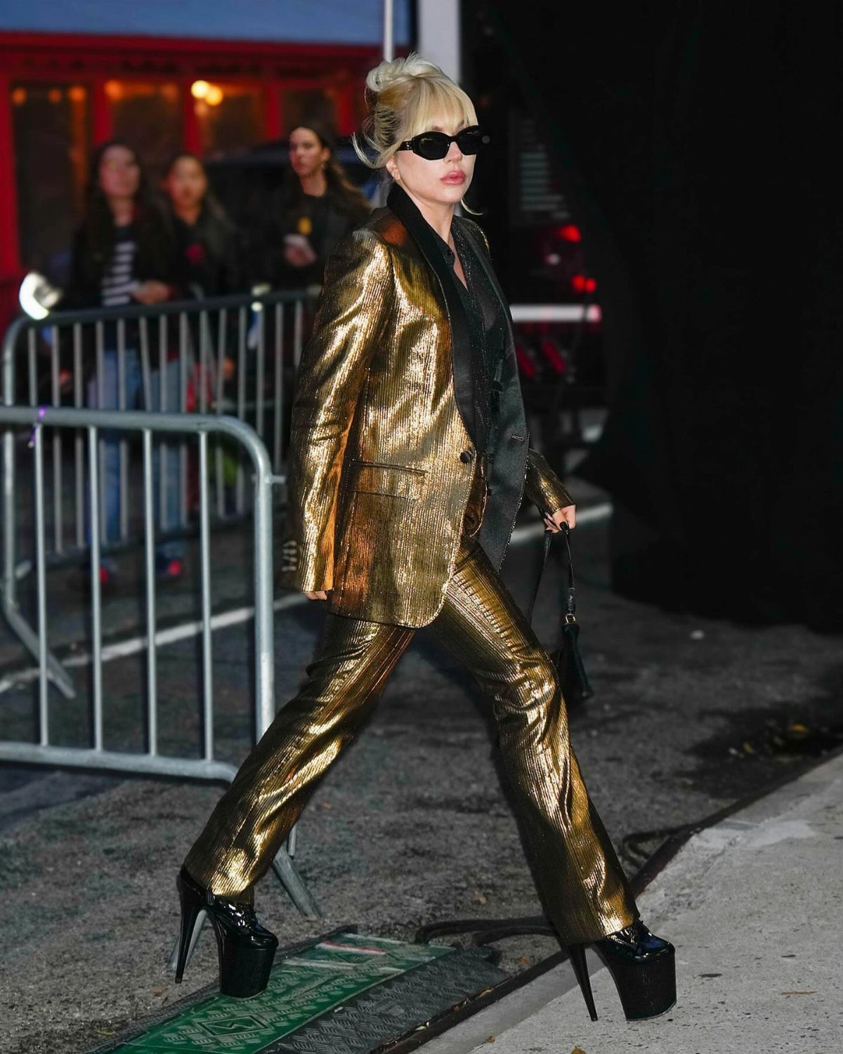 11 Lady Gaga Outfits That Defined Her Style Evolution 8 Lady Gaga wearing a metallic gold suit and black platform heels walking outdoors.