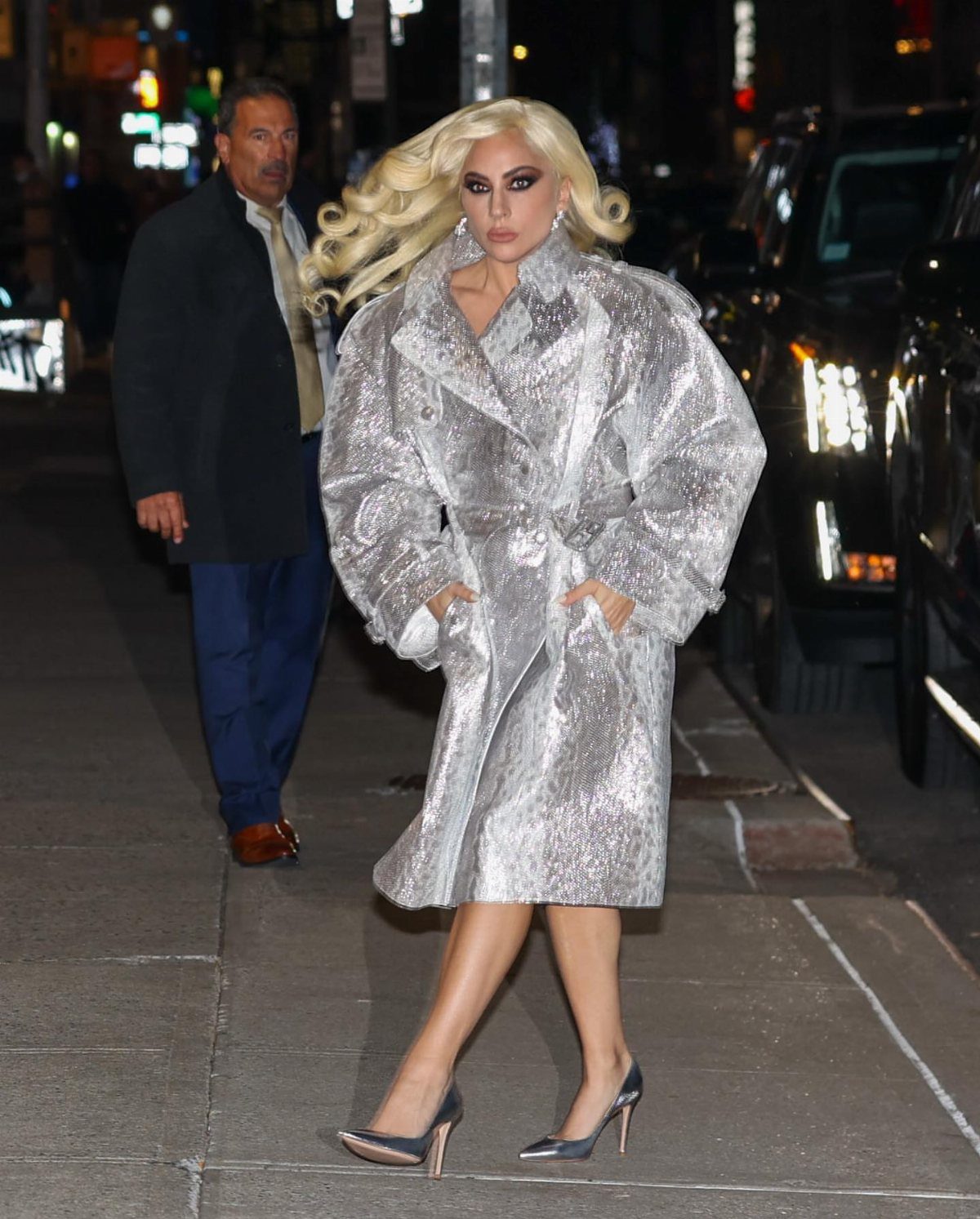 11 Lady Gaga Outfits That Defined Her Style Evolution 5 Lady Gaga wearing a shimmering oversized silver metallic coat and silver high heels.