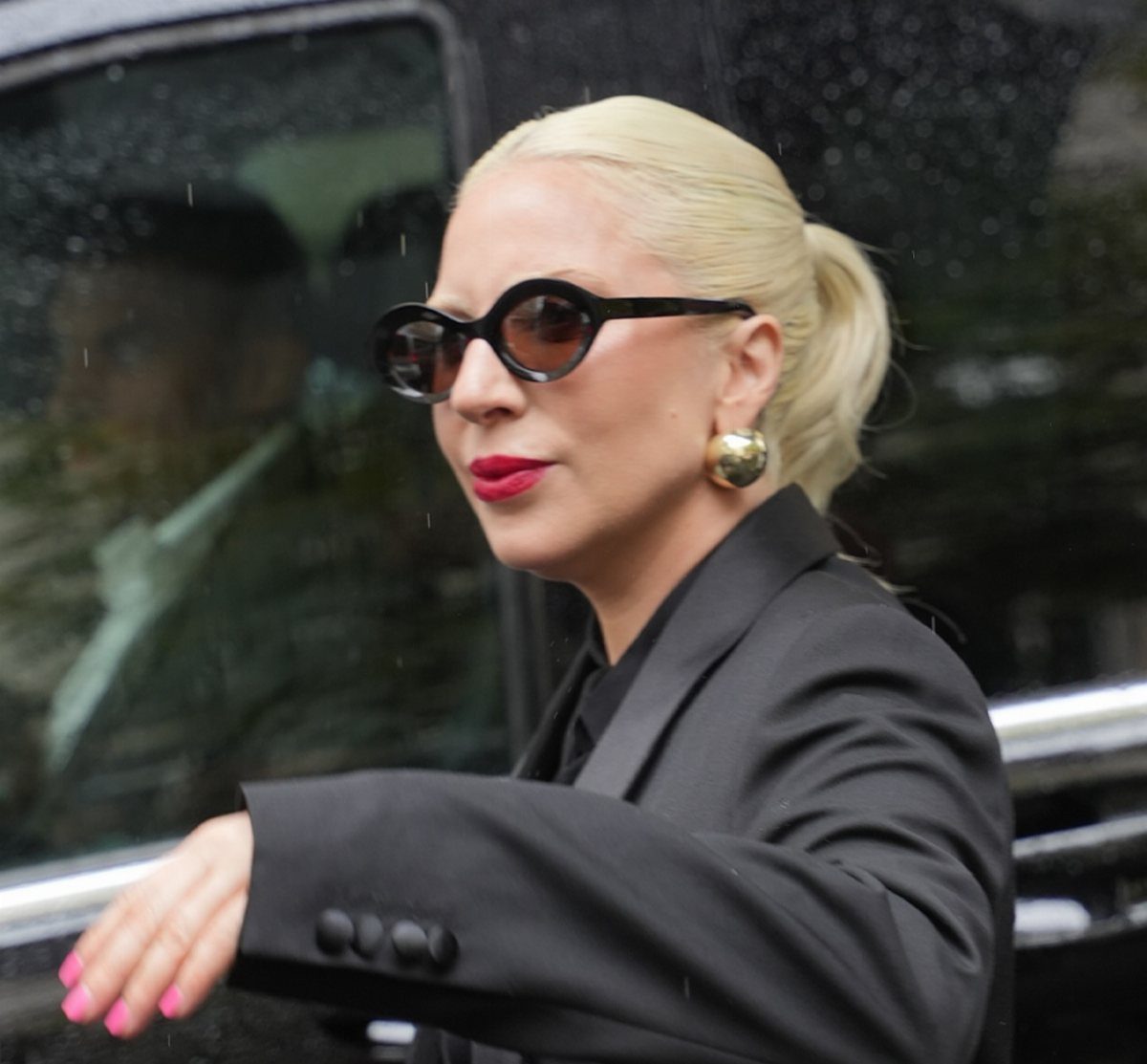 11 Lady Gaga Outfits That Defined Her Style Evolution 2 Lady Gaga wearing black sunglasses and a black blazer with gold earrings.