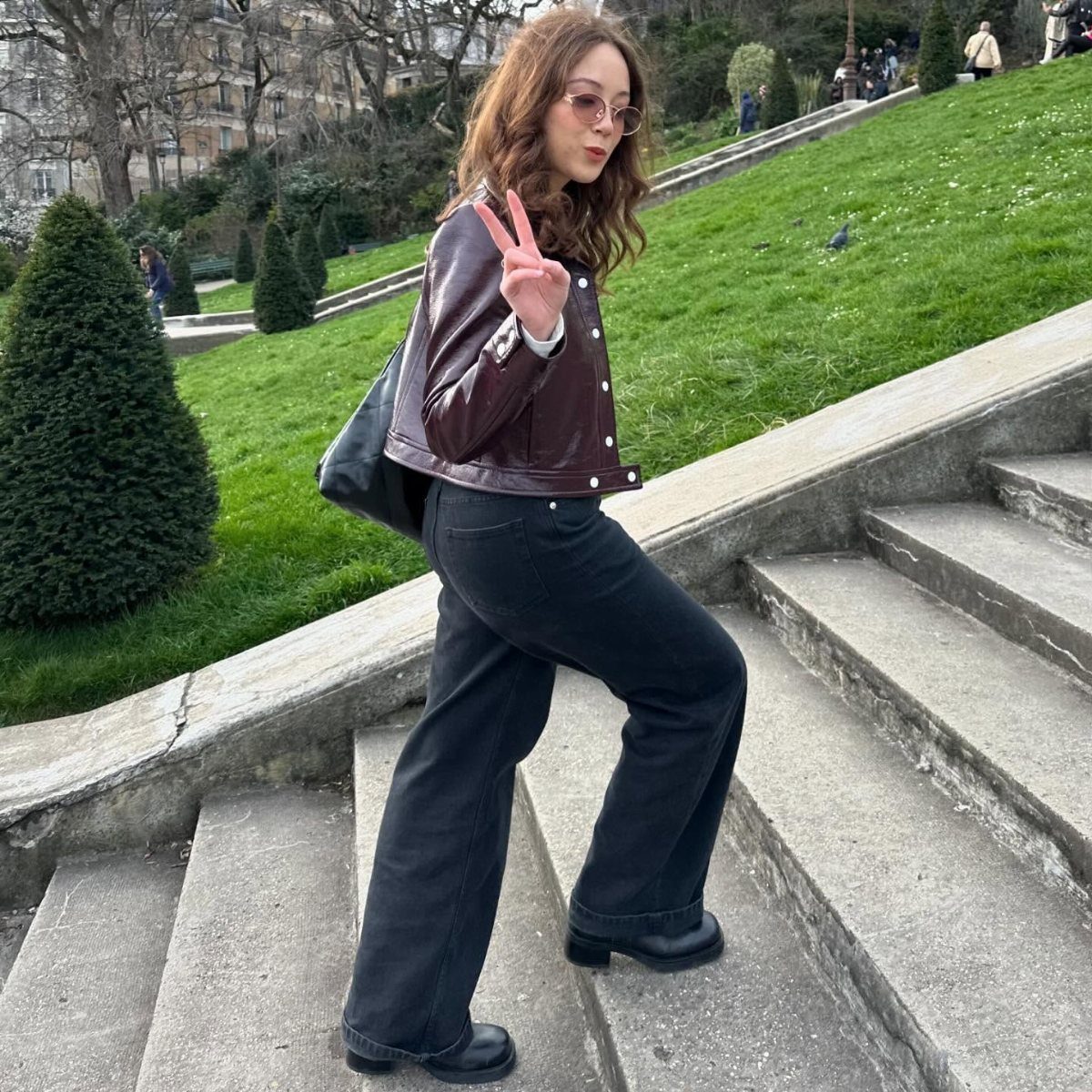 13 Laufey Concert Outfit Ideas for a Whimsical Night Out 8 Woman in burgundy leather jacket and black wide-leg trousers posing on stone stairs.