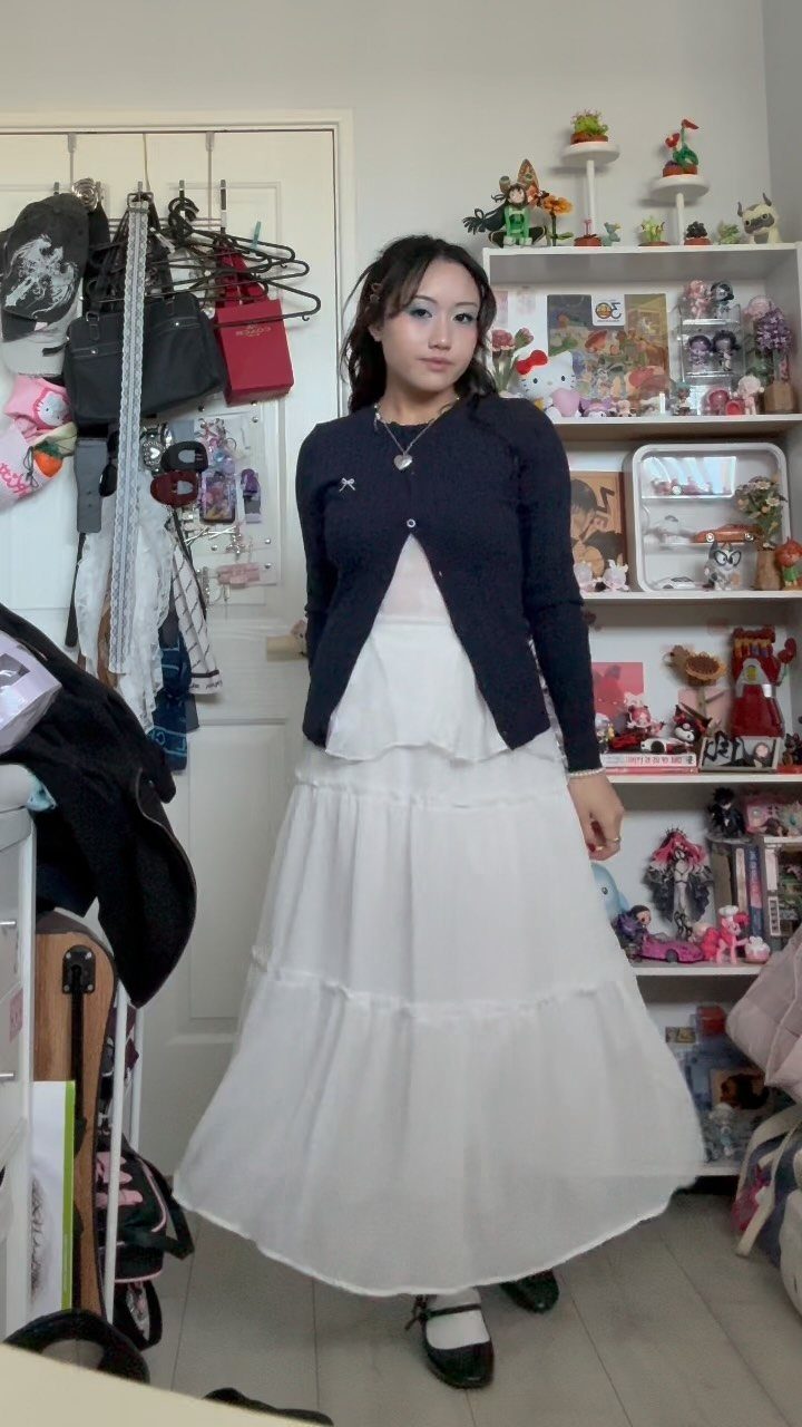 13 Laufey Concert Outfit Ideas for a Whimsical Night Out 11 Woman wearing a navy cardigan and tiered white maxi skirt for a concert outfit.
