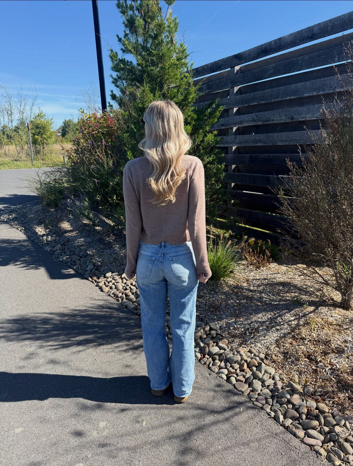 13 Laufey Concert Outfit Ideas for a Whimsical Night Out 9 Woman from behind wearing a brown cropped cardigan and straight-leg blue jeans.