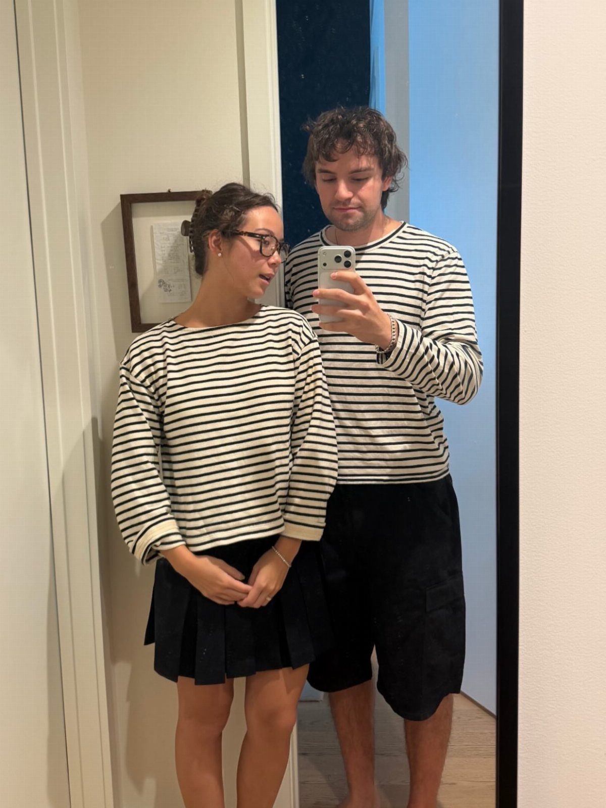 13 Laufey Concert Outfit Ideas for a Whimsical Night Out 7 Woman in striped top and black pleated skirt posing for a mirror selfie.