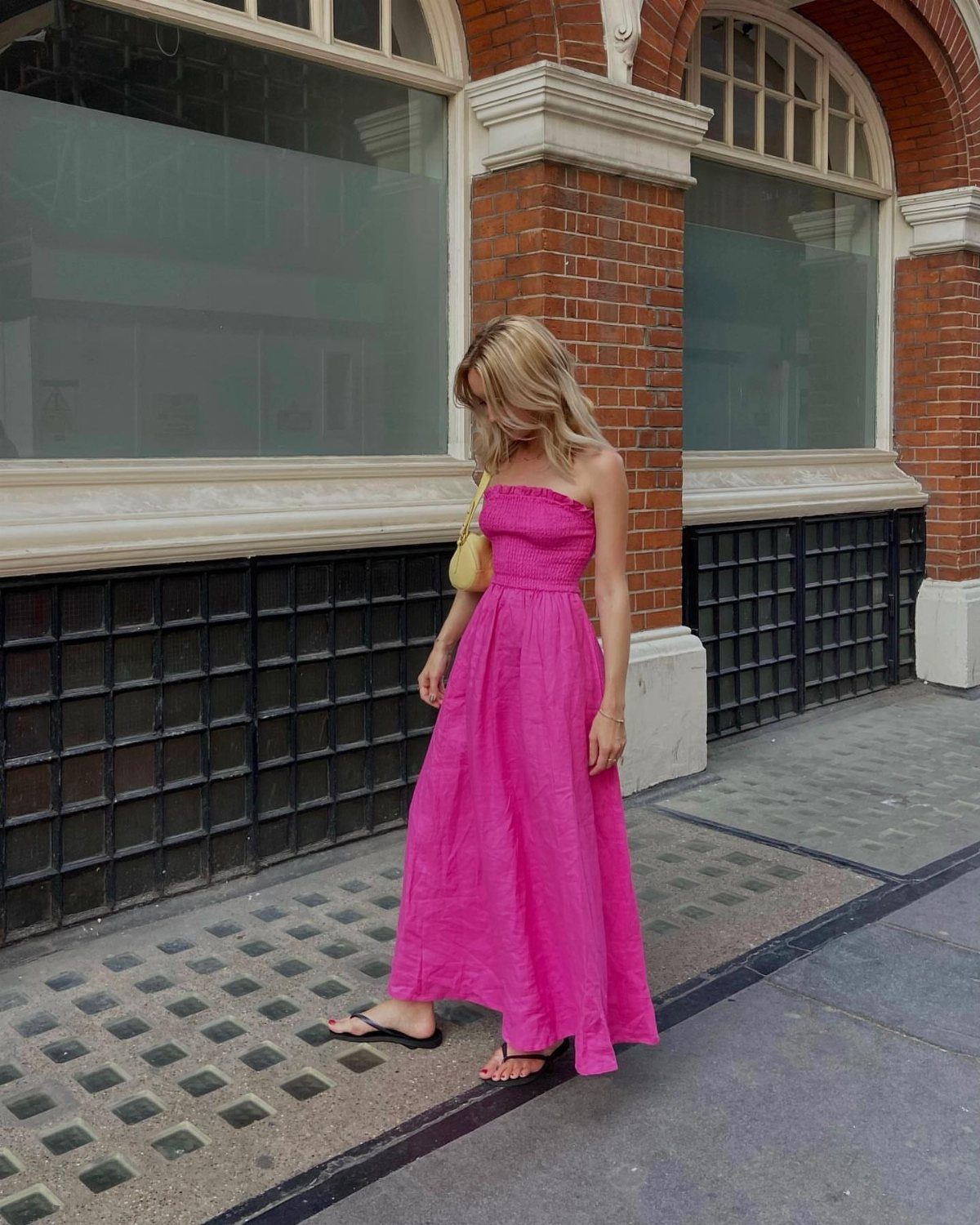10 Legally Blonde Outfits to Channel Elle Woods in 2026 6 Woman in a long strapless bright pink sundress standing by a brick building.