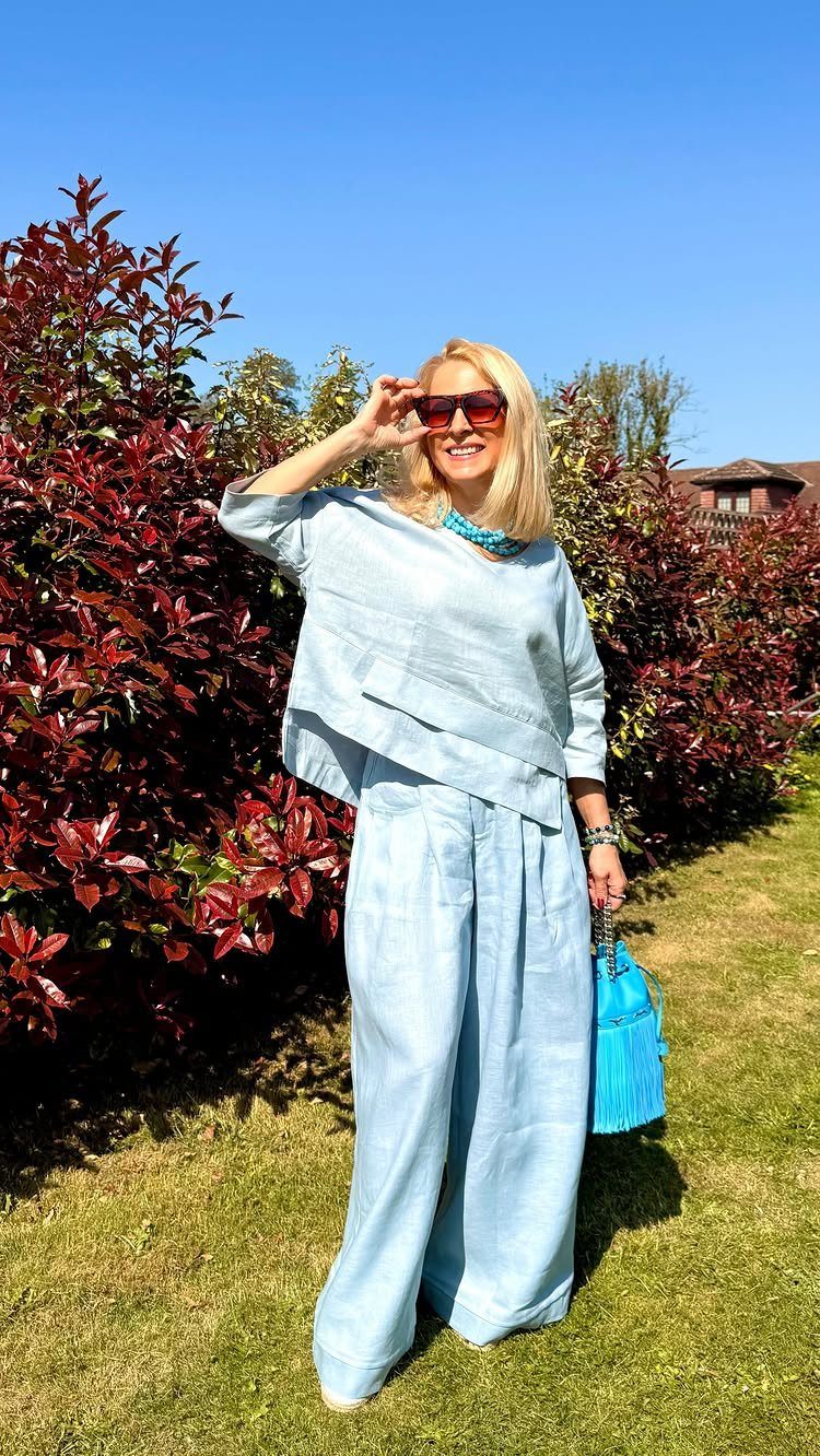 Light Summer Outfits: 8 Fresh Ideas for Cool, Soft Style 7 Woman in a light blue linen outfit with a blue handbag standing outdoors.