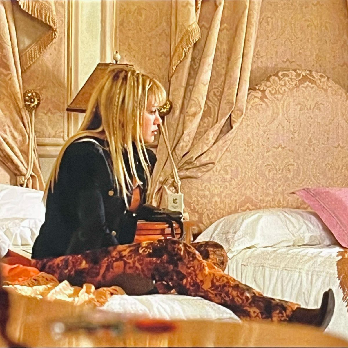 10 Lizzie McGuire Movie Outfits That Defined Y2K Fashion 9 Young woman with blonde braids wearing a black cardigan and patterned trousers on a bed