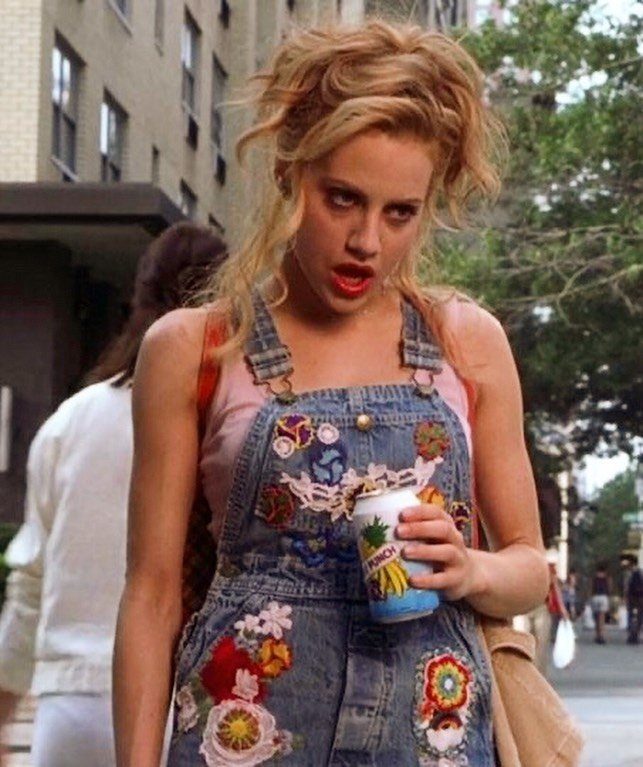 10 Lizzie McGuire Movie Outfits That Defined Y2K Fashion 4 Woman in floral embroidered denim overalls holding a drink on a city street.