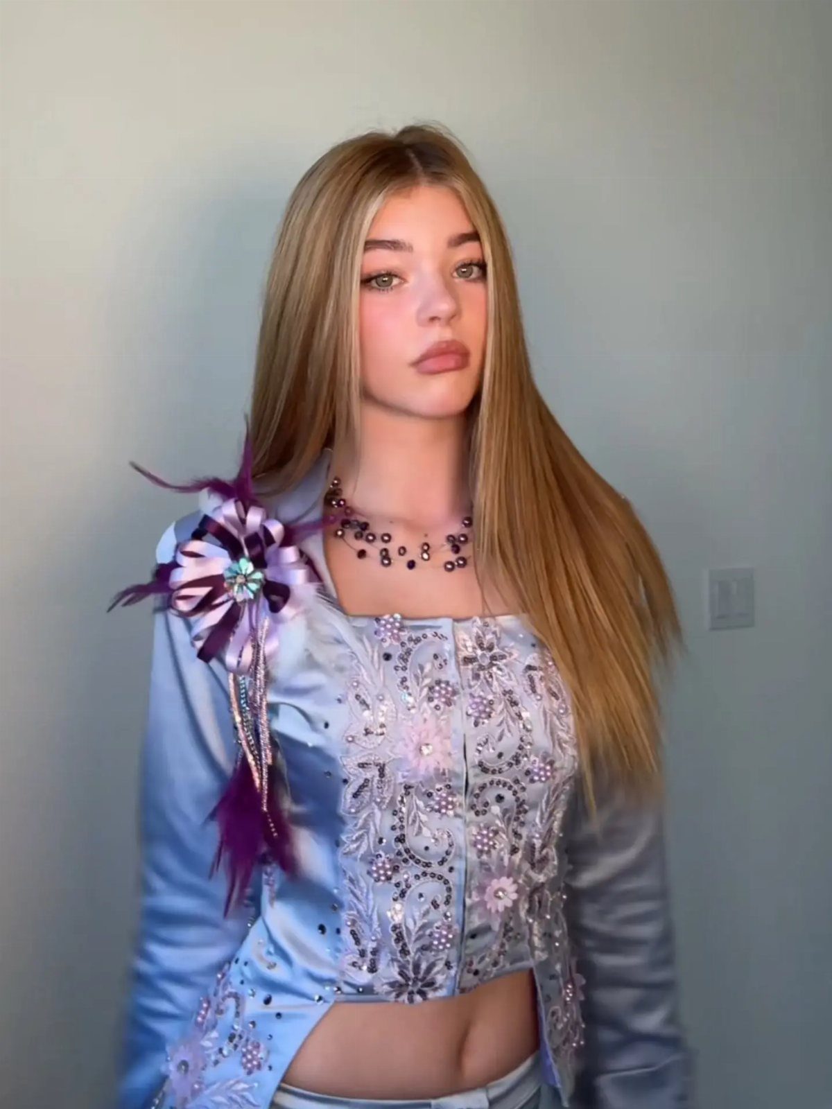 10 Lizzie McGuire Movie Outfits That Defined Y2K Fashion 7 Young woman wearing a light blue satin outfit with purple floral embroidery and feathers.