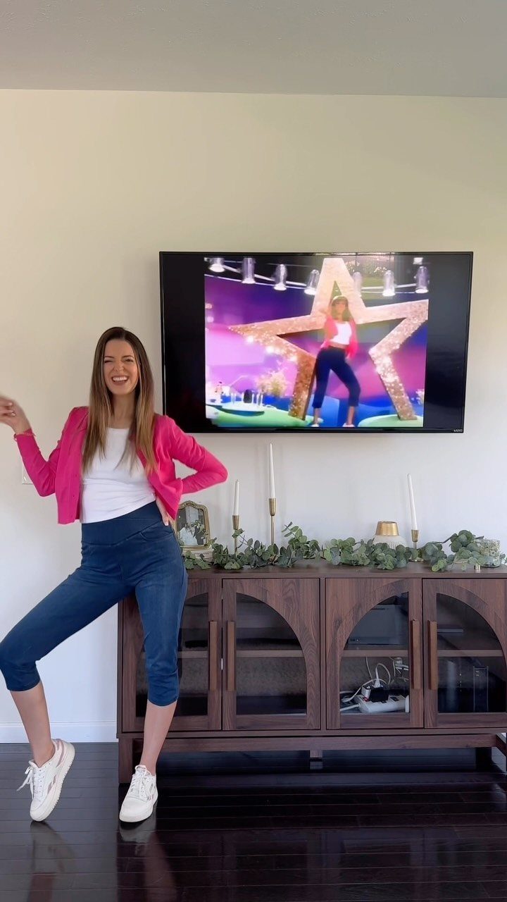10 Lizzie McGuire Movie Outfits That Defined Y2K Fashion 3 Woman posing in pink jacket and blue pants in front of a television.