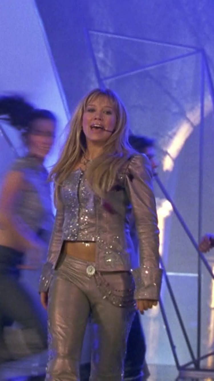 10 Lizzie McGuire Movie Outfits That Defined Y2K Fashion 5 Woman in a shimmering silver cropped jacket and matching trousers performing on stage.