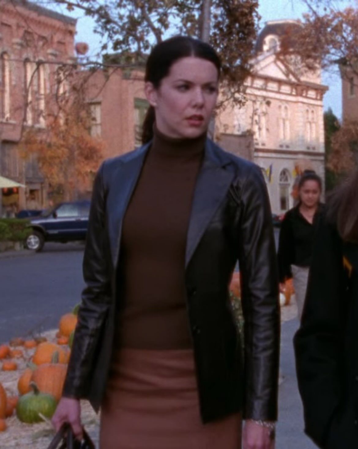 11 Lorelai Gilmore Outfits to Recreate Her Iconic Style 2 Woman wearing a black leather blazer, brown turtleneck, and brown pencil skirt outdoors.