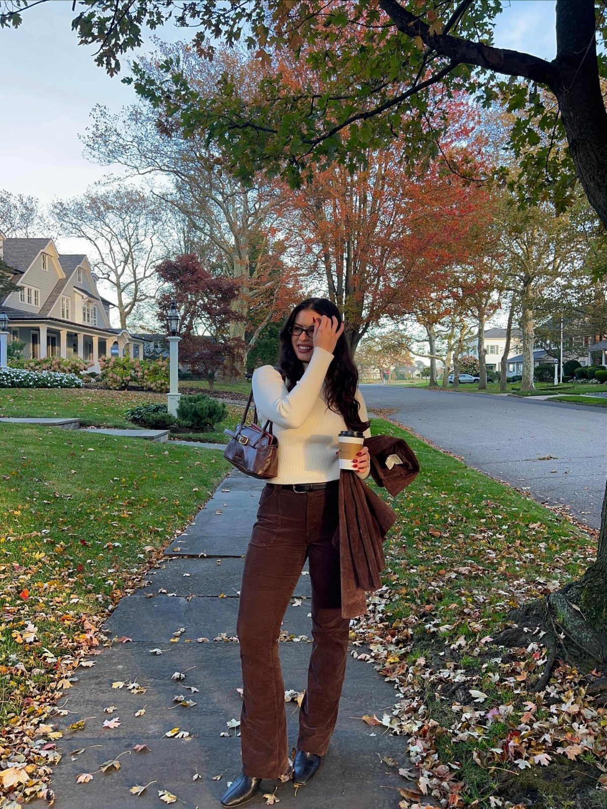 11 Lorelai Gilmore Outfits to Recreate Her Iconic Style 6 Woman wearing a white top and brown flared pants on a fall sidewalk