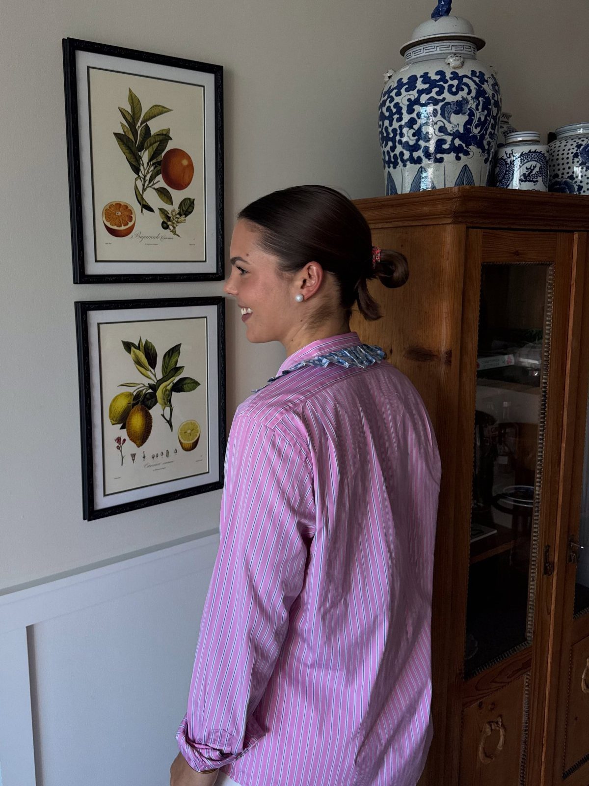 11 Lorelai Gilmore Outfits to Recreate Her Iconic Style 11 Woman wearing a pink patterned button-down shirt standing next to botanical wall art.