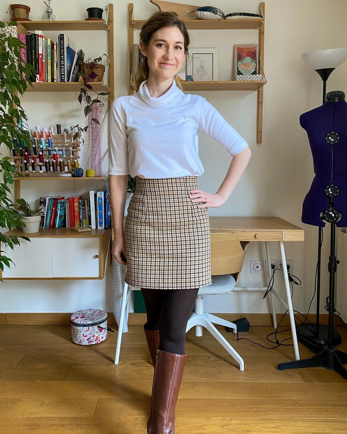 11 Lorelai Gilmore Outfits to Recreate Her Iconic Style 4 Woman wearing a white turtleneck, brown checkered pencil skirt, and brown knee-high boots.