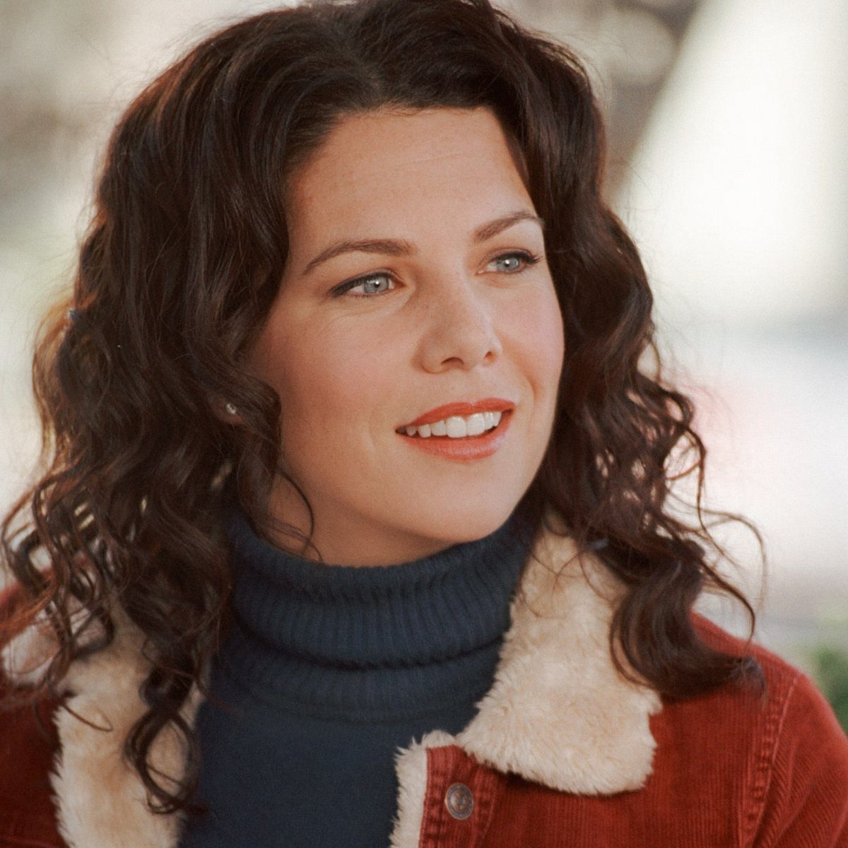 11 Lorelai Gilmore Outfits to Recreate Her Iconic Style 1 Woman with curly brown hair wearing a dark blue turtleneck and rust corduroy jacket.