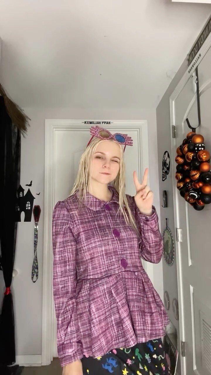 Person wearing purple plaid top and pink spectrespecs posing in a decorated room.