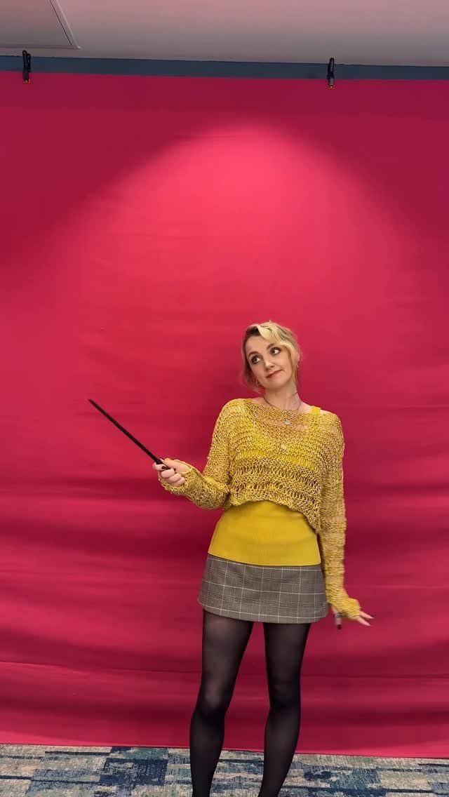Woman in yellow crochet sweater and plaid skirt holding a magic wand.