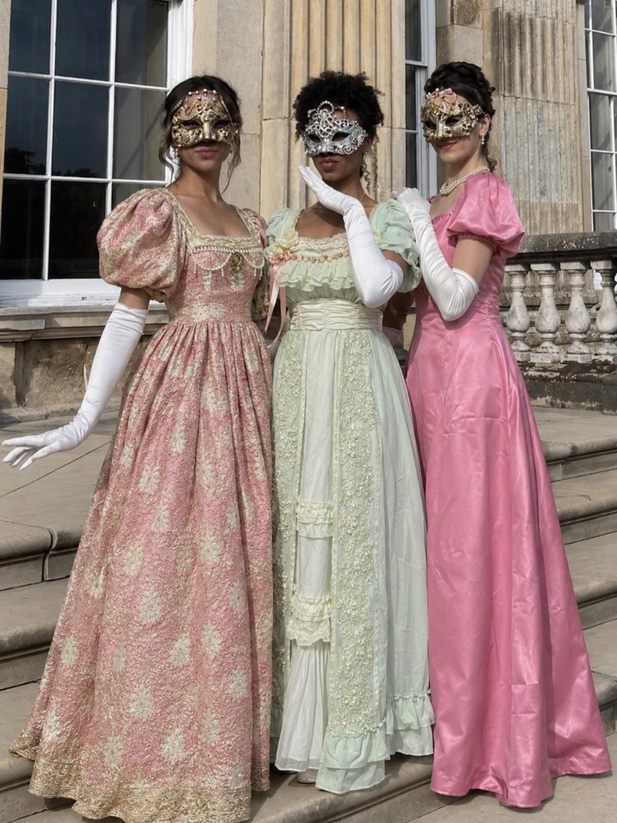 10 Stunning Masquerade Outfits for Women to Wear This Year 1 Three women in floor-length gowns and ornate masquerade masks posing on stone steps.