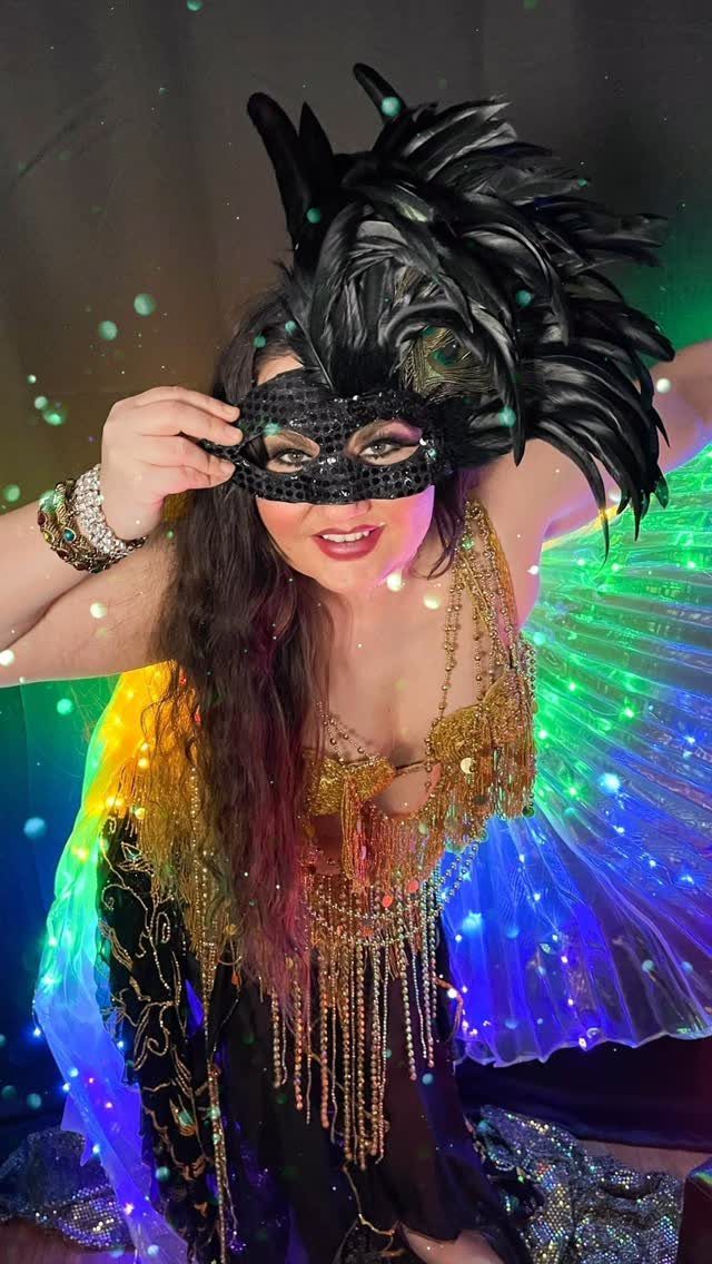 10 Stunning Masquerade Outfits for Women to Wear This Year 4 Woman in a gold beaded outfit and feathered mask with colorful glowing lights.
