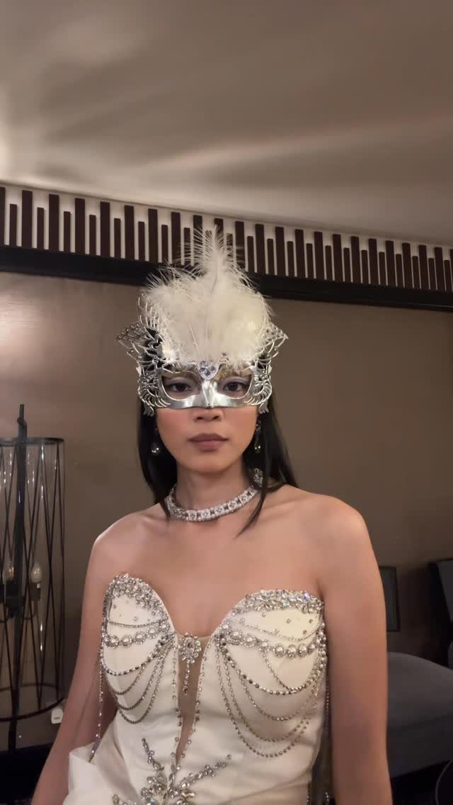 10 Stunning Masquerade Outfits for Women to Wear This Year 9 Woman in a white beaded gown and silver feathered masquerade mask posing indoors.