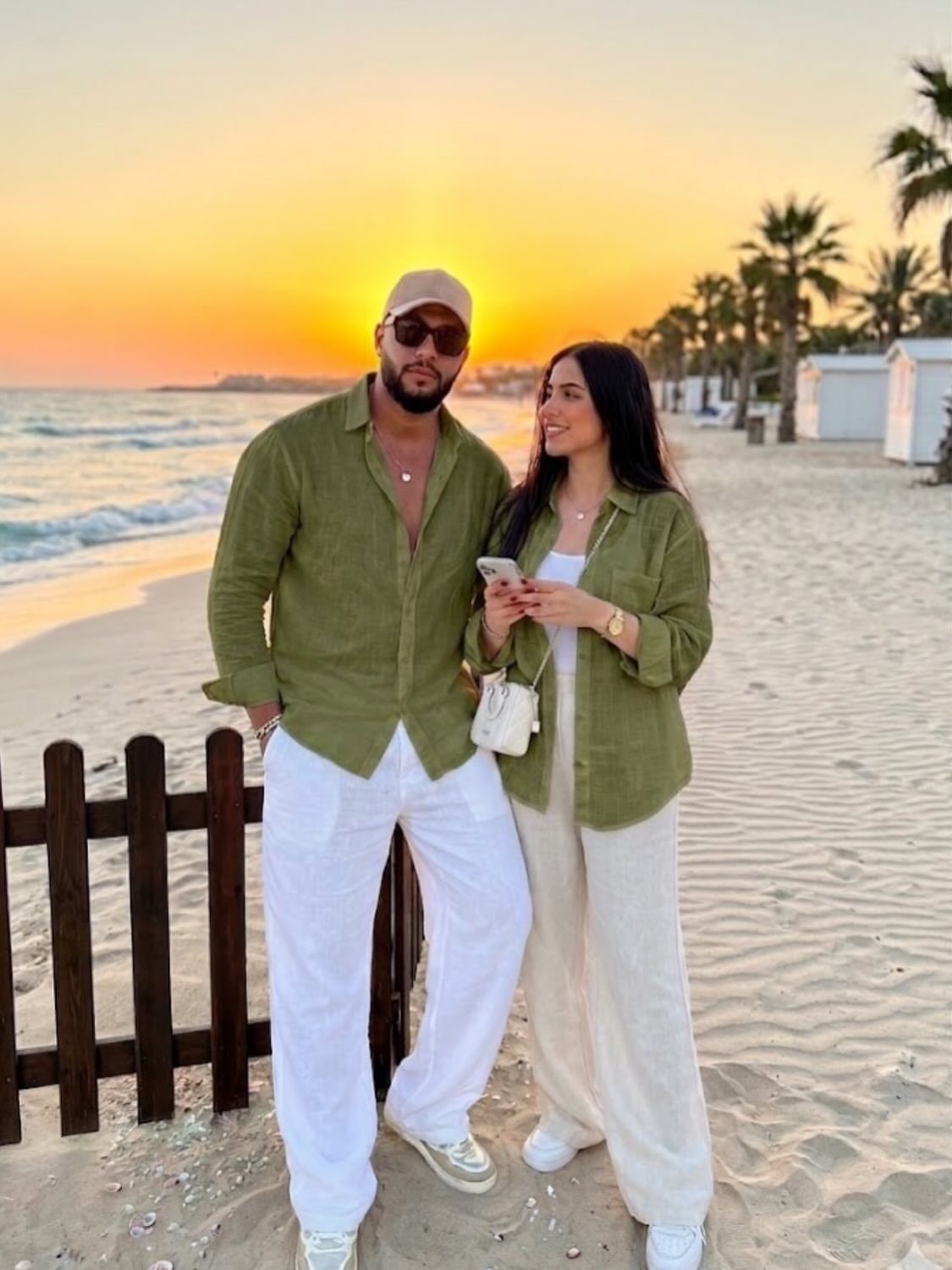 Matching Outfits for Couples: 6 Ideas from Gym to Formal 6 Couple wearing matching olive green linen shirts and white linen trousers on a beach.