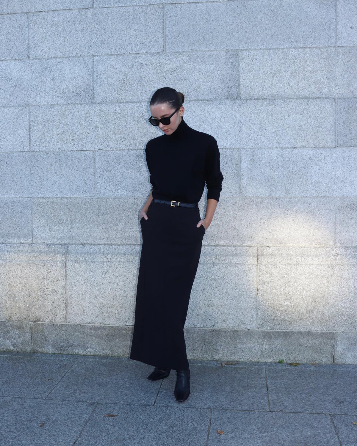 12 Maxi Skirt Outfits to Wear All Year in 2026 10 Woman in black turtleneck and black maxi skirt posing against a stone wall.