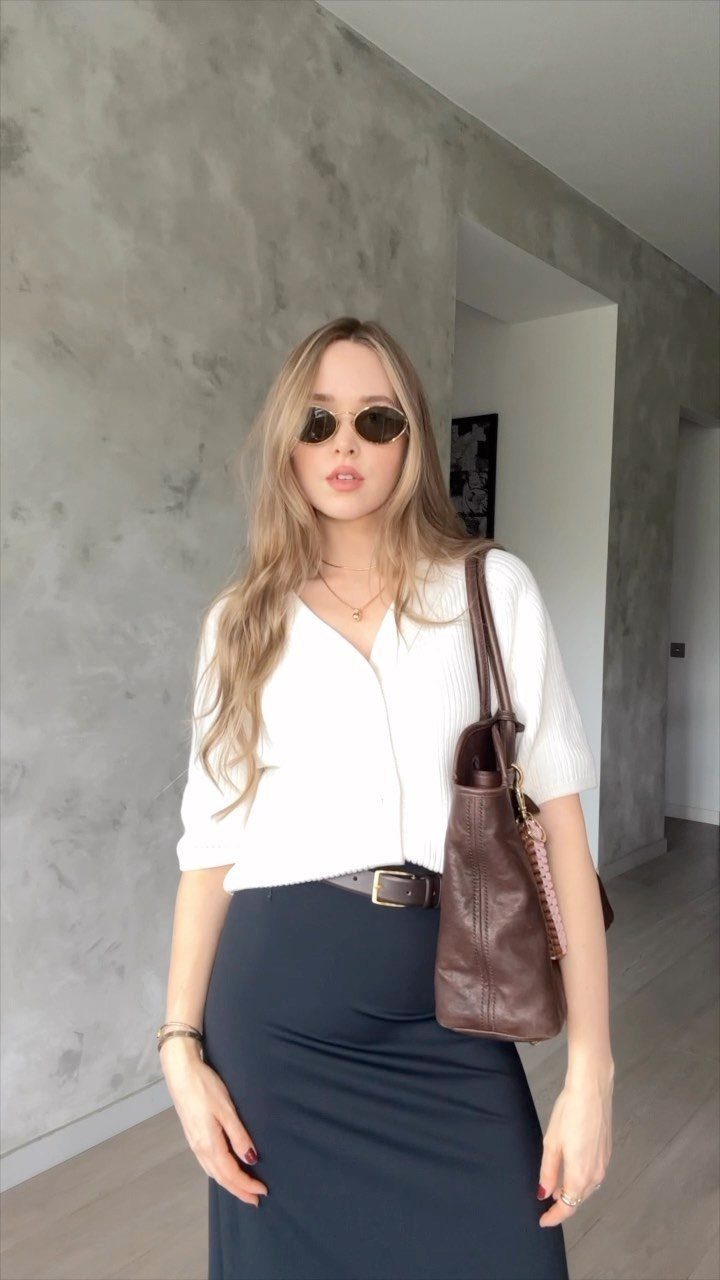 12 Maxi Skirt Outfits to Wear All Year in 2026 11 Woman wearing a white cardigan and black maxi skirt with a brown leather bag.