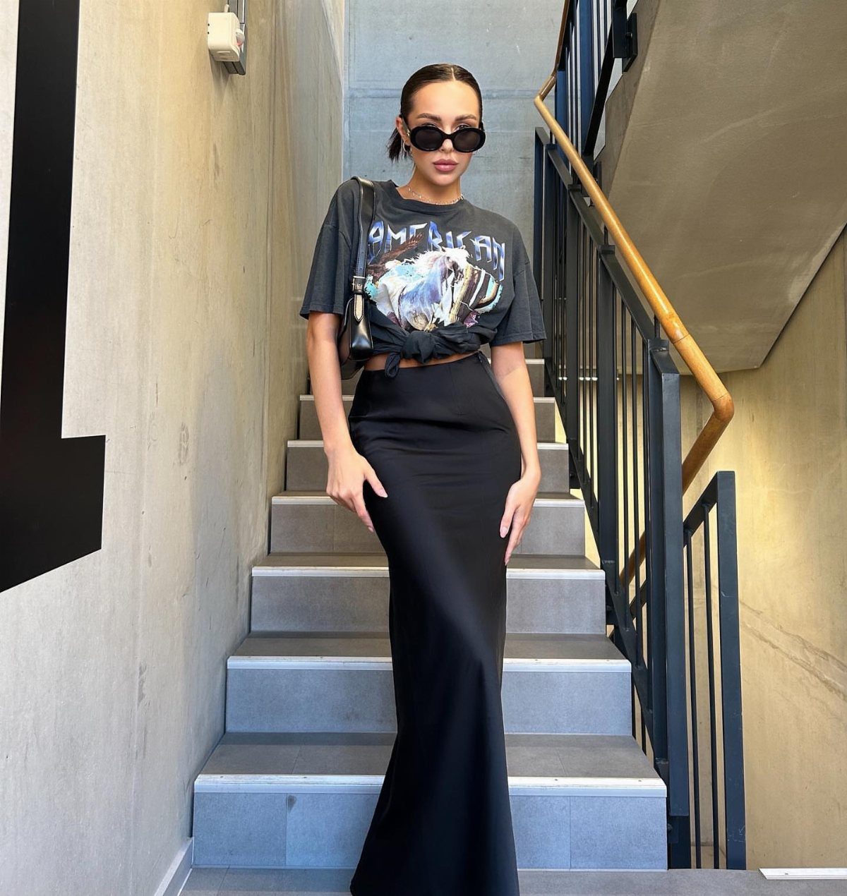 12 Maxi Skirt Outfits to Wear All Year in 2026 5 Woman in black maxi skirt and grey graphic tee standing on concrete stairs.
