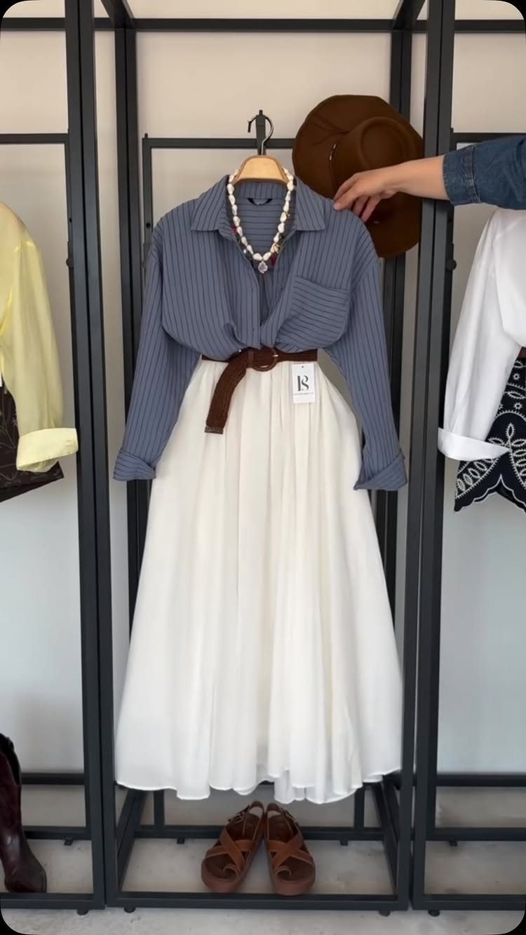 12 Maxi Skirt Outfits to Wear All Year in 2026 3 Striped blue button-down shirt and white maxi skirt displayed on a clothing rack.