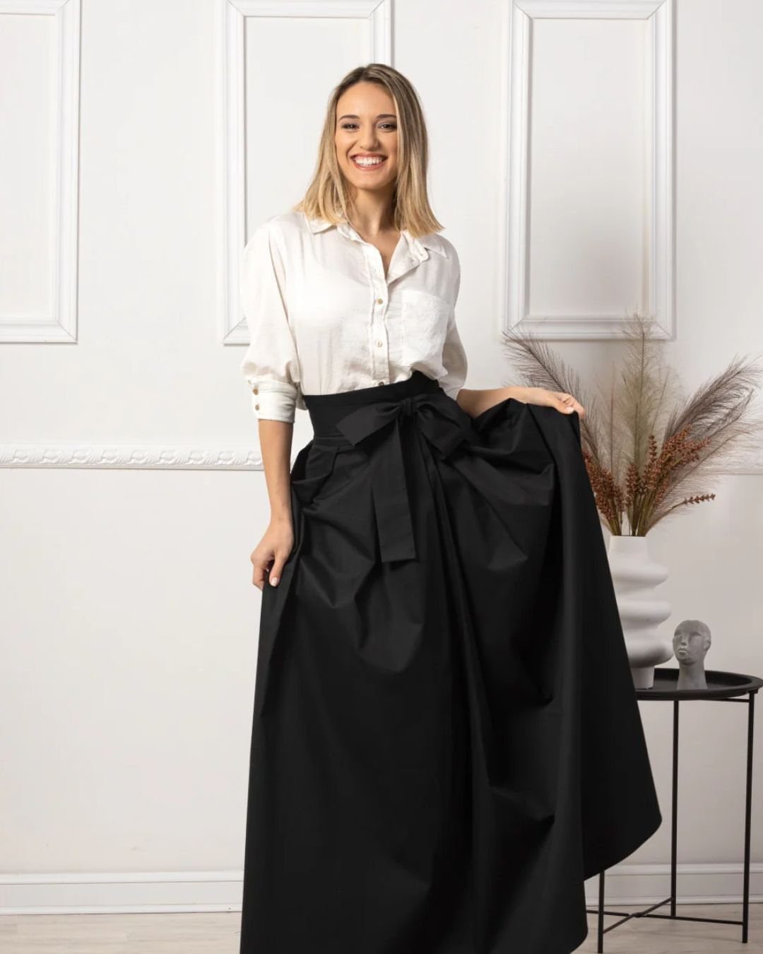 12 Maxi Skirt Outfits to Wear All Year in 2026 12 Woman in white button-down shirt and voluminous black maxi skirt with waist bow.