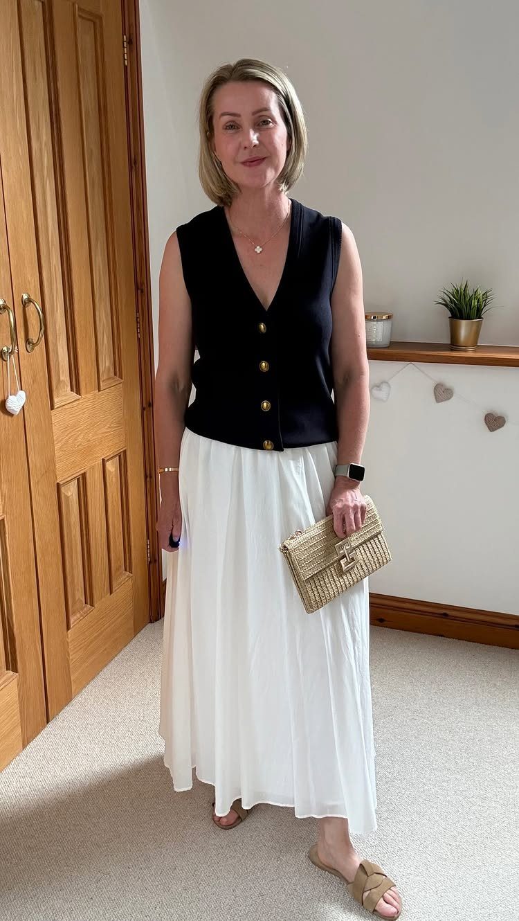 12 Maxi Skirt Outfits to Wear All Year in 2026 1 Woman wearing a black sleeveless top and a long white maxi skirt with straw clutch.