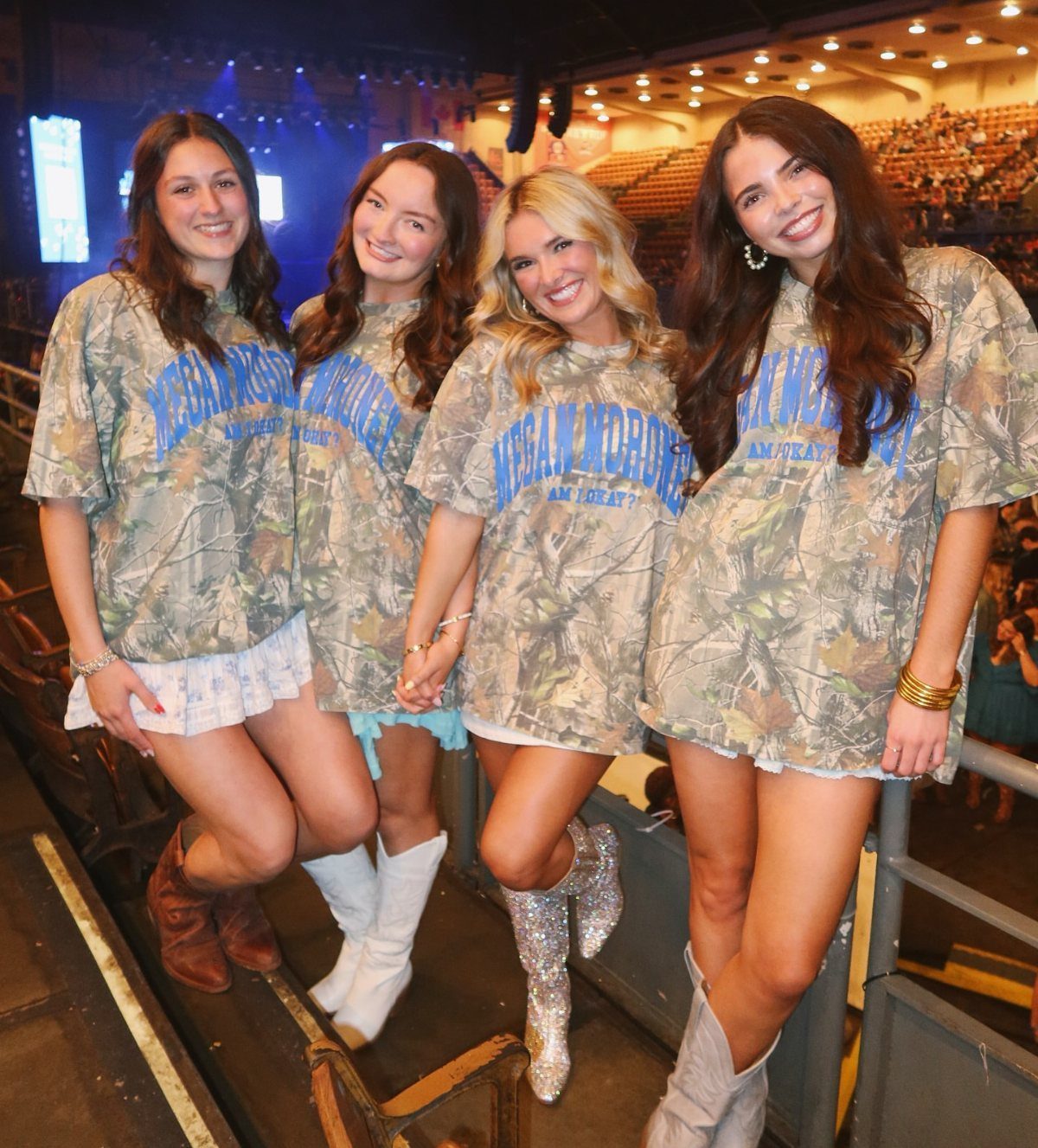 Megan Moroney Concert Outfits: 7 Ideas for Her Shows 6 Four women wearing camouflage graphic tees and short skirts at a concert venue.