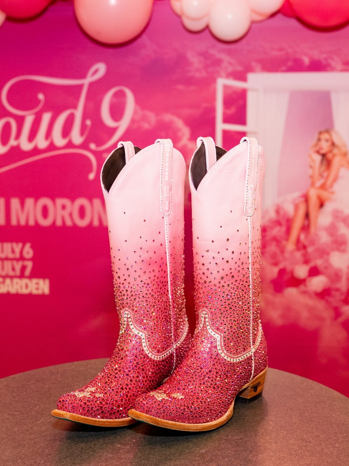 Megan Moroney Concert Outfits: 7 Ideas for Her Shows 4 Pink rhinestone cowboy boots with a gradient effect on a grey pedestal.