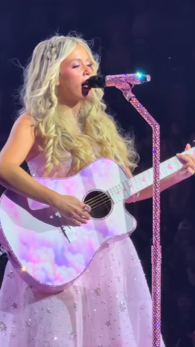 Megan Moroney Concert Outfits: 7 Ideas for Her Shows 7 Blonde woman in a pink sparkling dress playing a cloud-patterned acoustic guitar on stage.