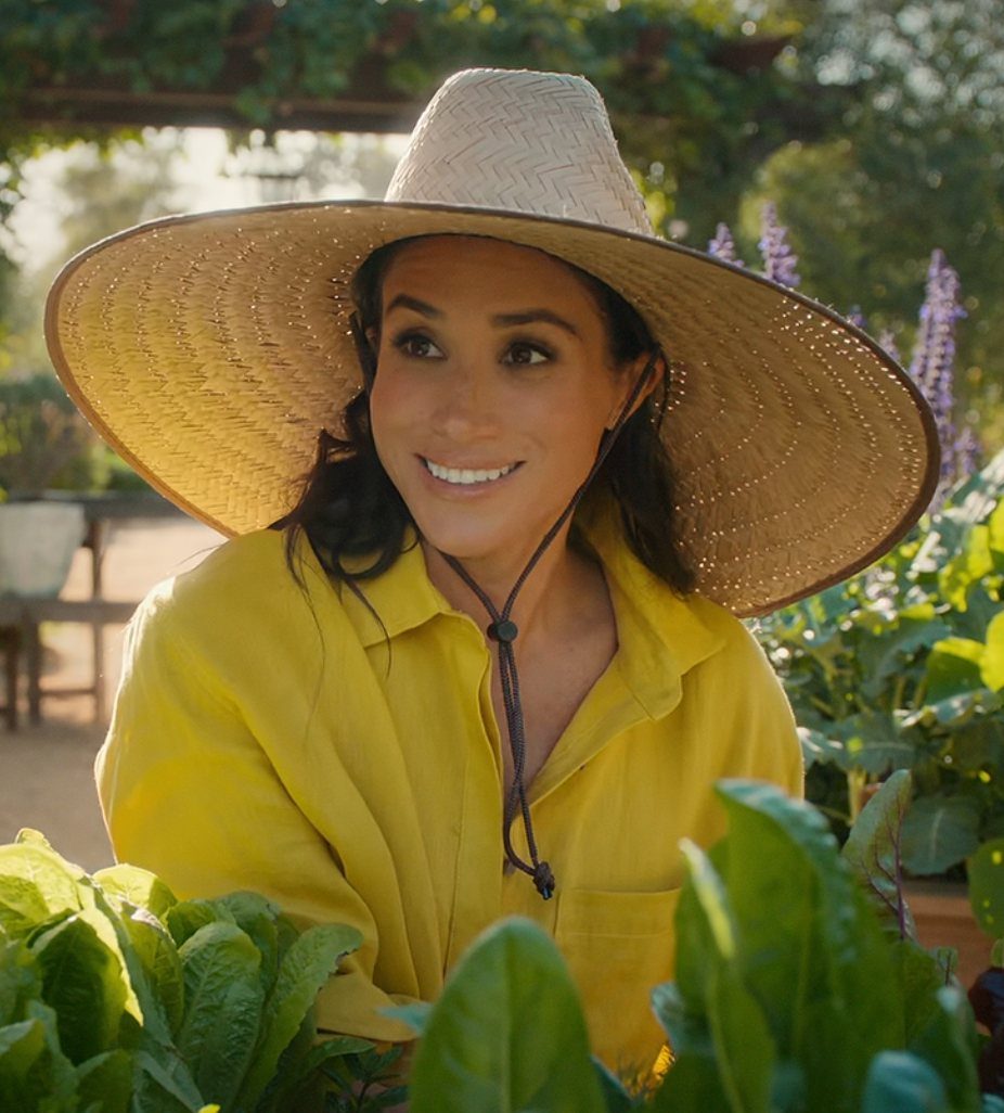 Meghan Markle Outfits: 17 Ideas from Tailored to Casual 15 Meghan Markle wearing a vibrant yellow shirt and straw hat in a garden.