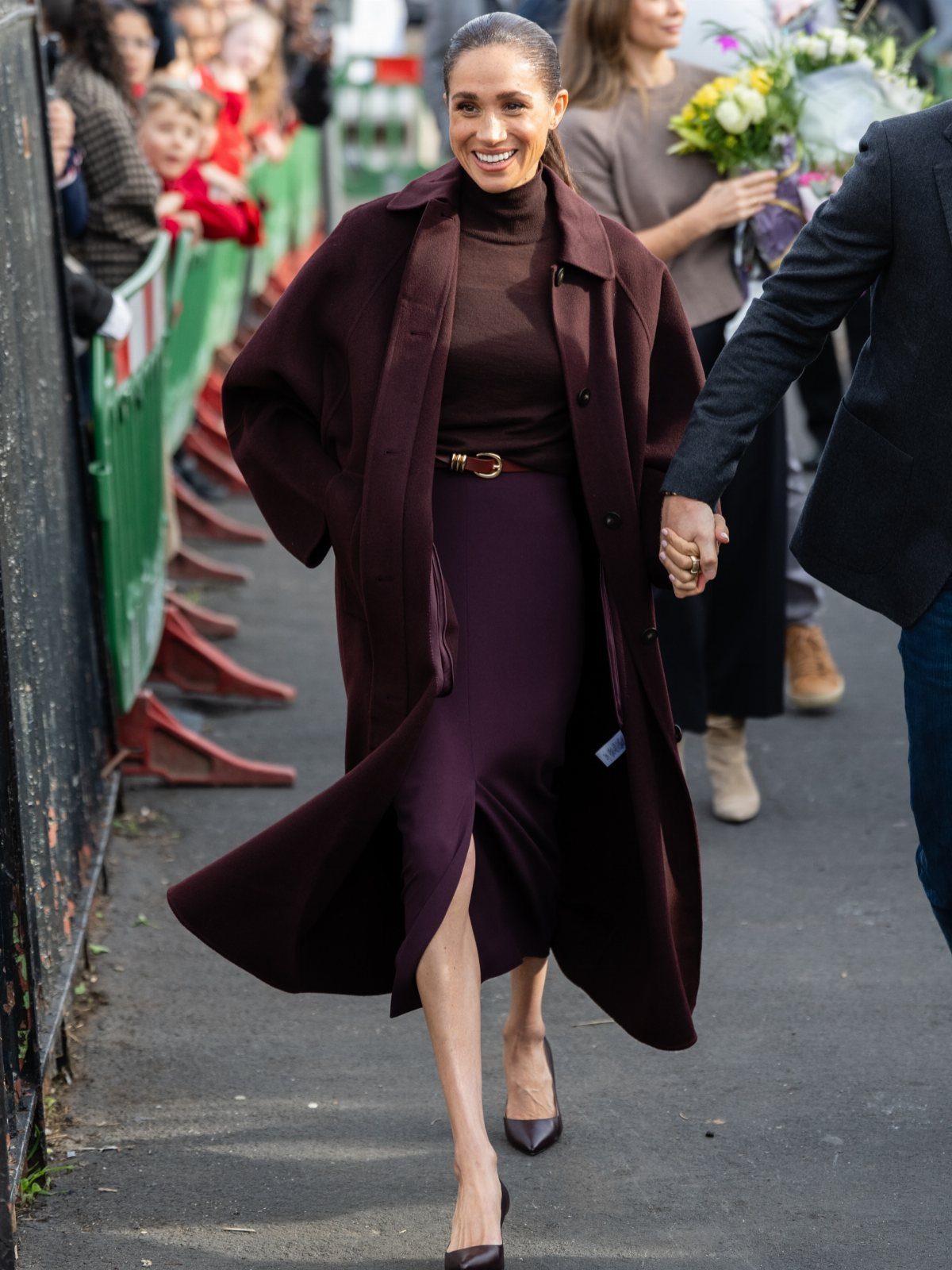 Meghan Markle Outfits: 17 Ideas from Tailored to Casual 6 Meghan Markle wearing a monochromatic burgundy oversized coat, turtleneck, and midi skirt.
