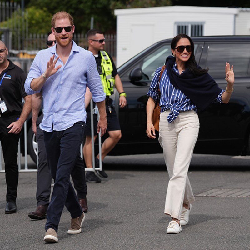 Meghan Markle Outfits: 17 Ideas from Tailored to Casual 11 Meghan Markle wearing a striped blue shirt, white trousers, and white sneakers walking outdoors.