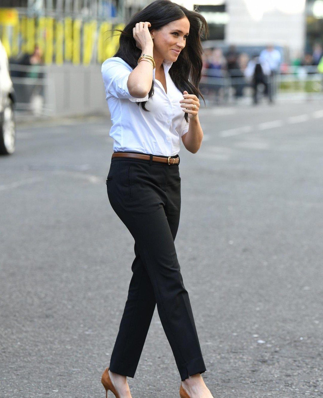 Meghan Markle Outfits: 17 Ideas from Tailored to Casual 16 Meghan Markle wearing a white button-down shirt and black tailored trousers on a street.