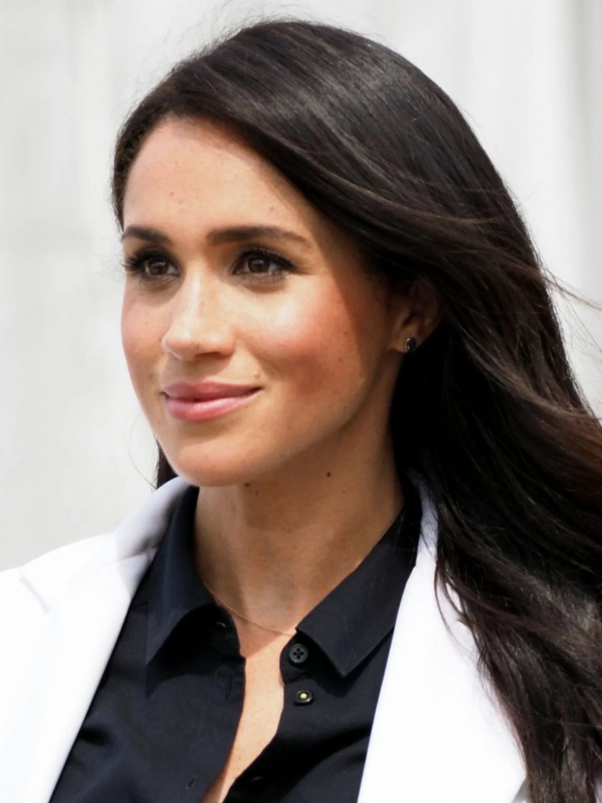Meghan Markle Outfits: 17 Ideas from Tailored to Casual 13 Meghan Markle wearing a white blazer and black collared shirt with long dark hair.