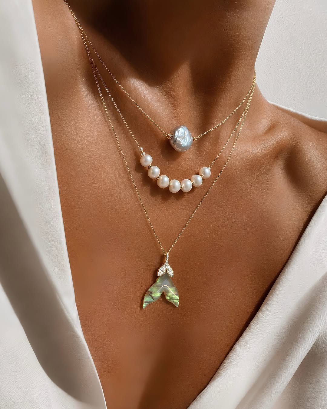 Mermaid Inspired Outfits for Your 5 Most Magical Looks 4 Three layered gold necklaces with pearls and a mermaid tail pendant on a person.