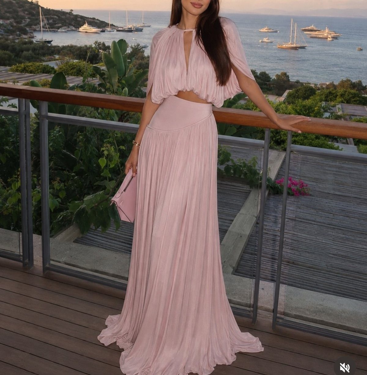 Mermaid Inspired Outfits for Your 5 Most Magical Looks 3 Woman in a light pink pleated halter crop top and maxi skirt on a deck.