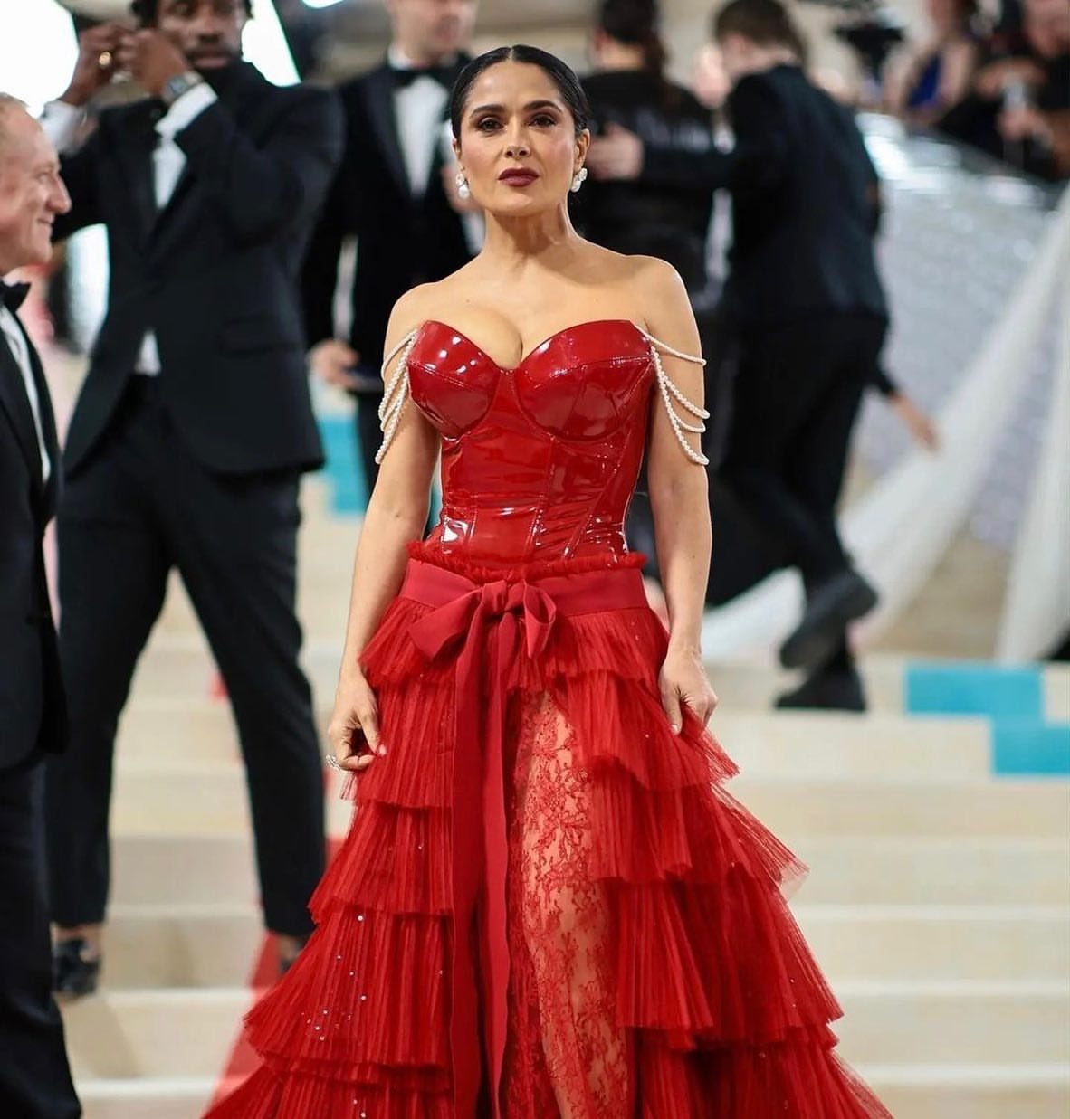 Met Gala Outfits 2026: 10 Looks That Stole the Night 5 Woman in a red latex and tulle gown posing on stairs at an event.