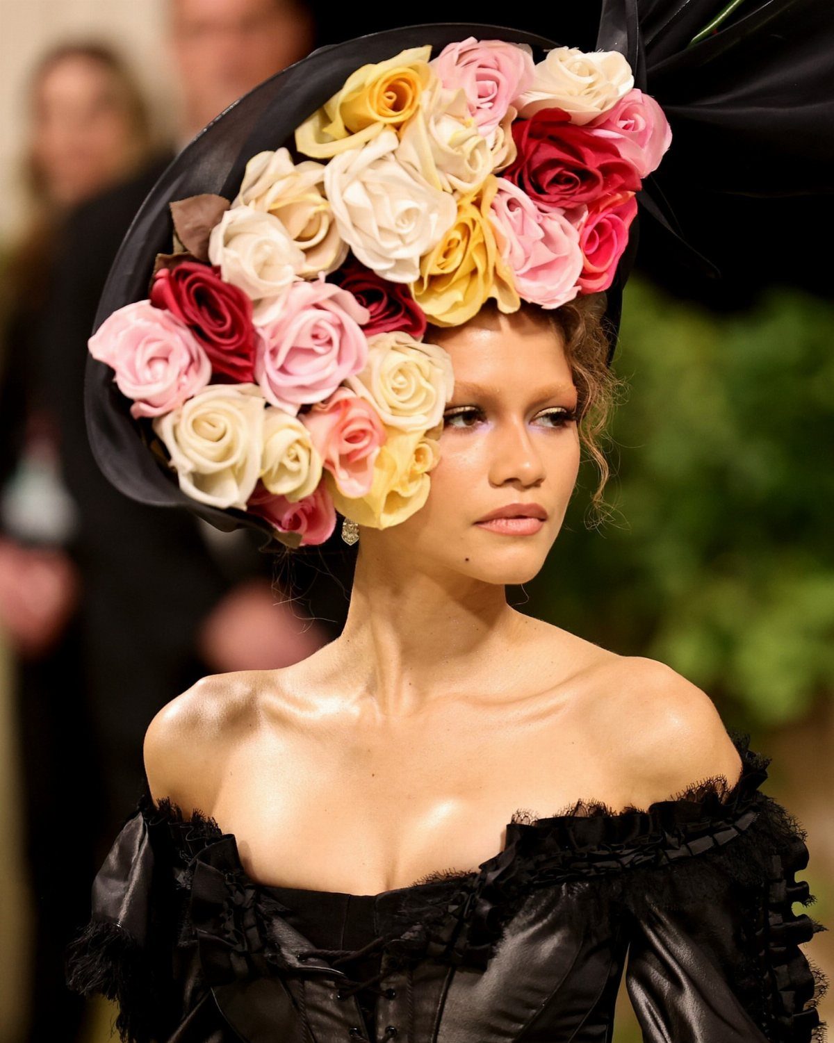 Met Gala Outfits 2026: 10 Looks That Stole the Night 2 Woman in a black dress wearing a hat covered in colorful roses.