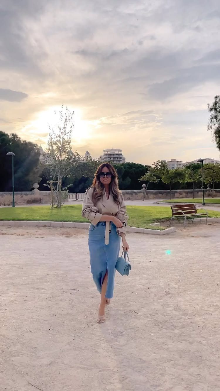 12 Midi Skirt Outfits for Every Season and Style 6 Woman wearing a beige button-down shirt and blue denim midi skirt walking outdoors.