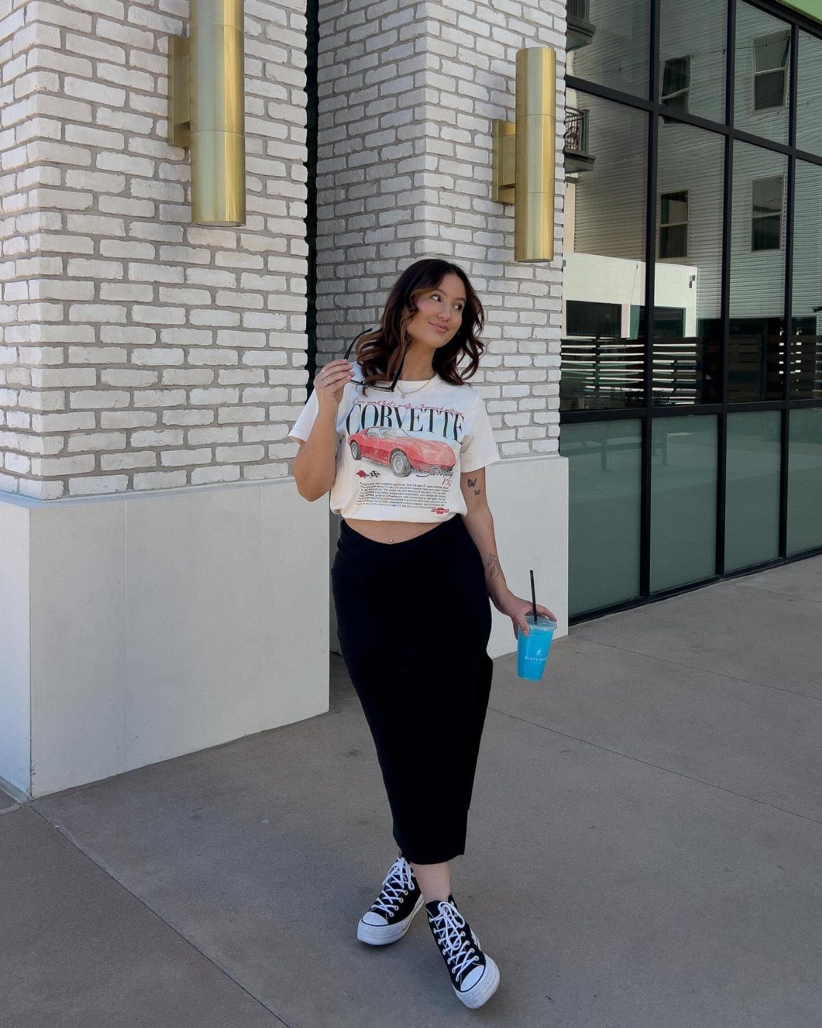 12 Midi Skirt Outfits for Every Season and Style 10 Woman wearing a white graphic t-shirt, black midi skirt, and black sneakers outdoors.