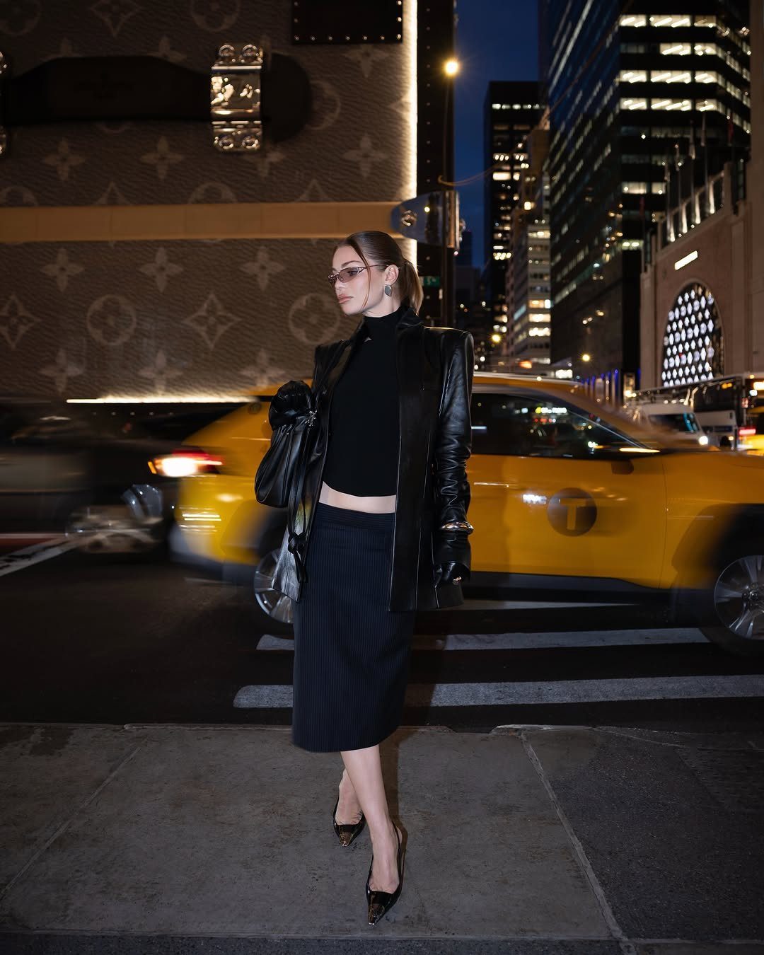 12 Midi Skirt Outfits for Every Season and Style 2 Woman wearing a black leather jacket and black midi skirt on a city street.