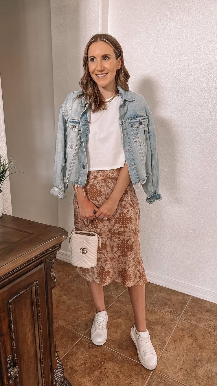 12 Midi Skirt Outfits for Every Season and Style 1 Woman wearing a white t-shirt, denim jacket, brown patterned midi skirt and white sneakers.