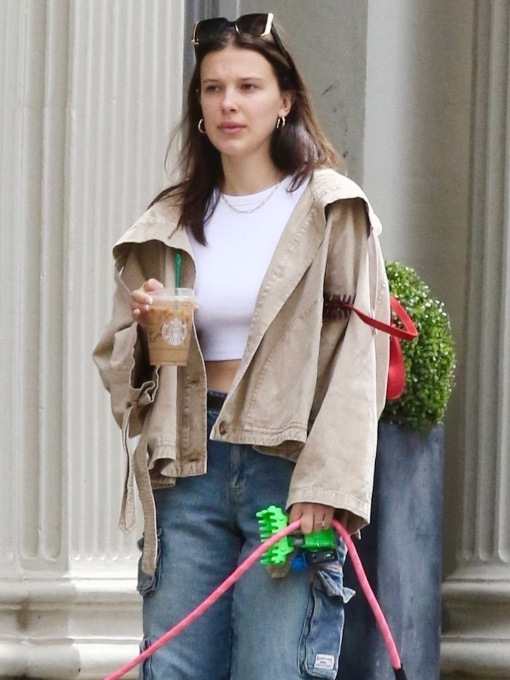 15 Millie Bobby Brown Outfits to Inspire Your Wardrobe 10 Millie Bobby Brown in a white crop top, tan jacket, and blue cargo jeans.